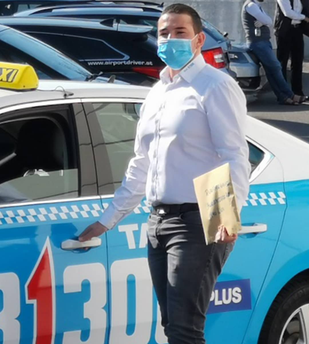 Taxilenker mit MNS-Maske vor Taxi